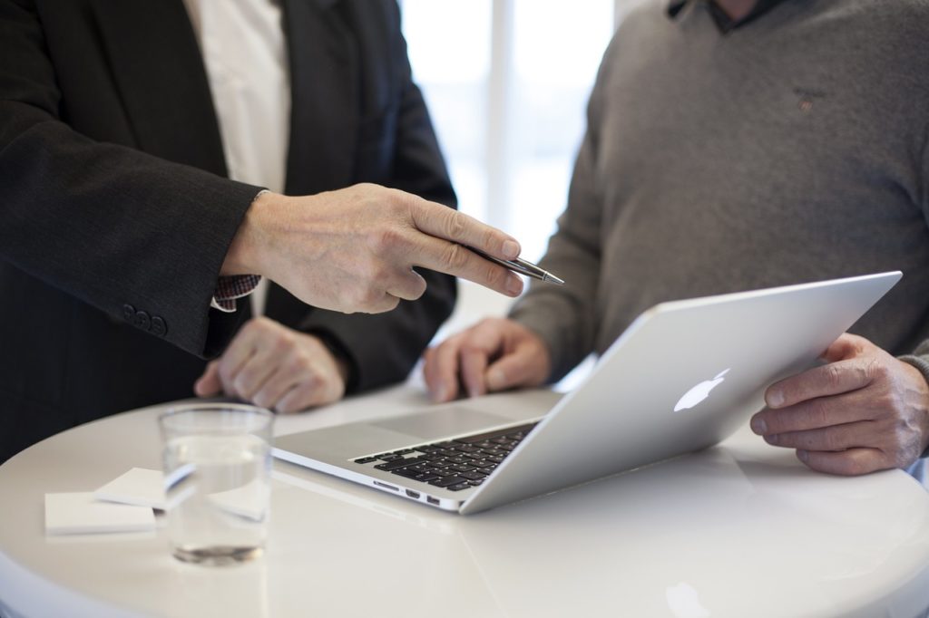 Dos empresarios hablando mientras uno señala al macbook del otro.